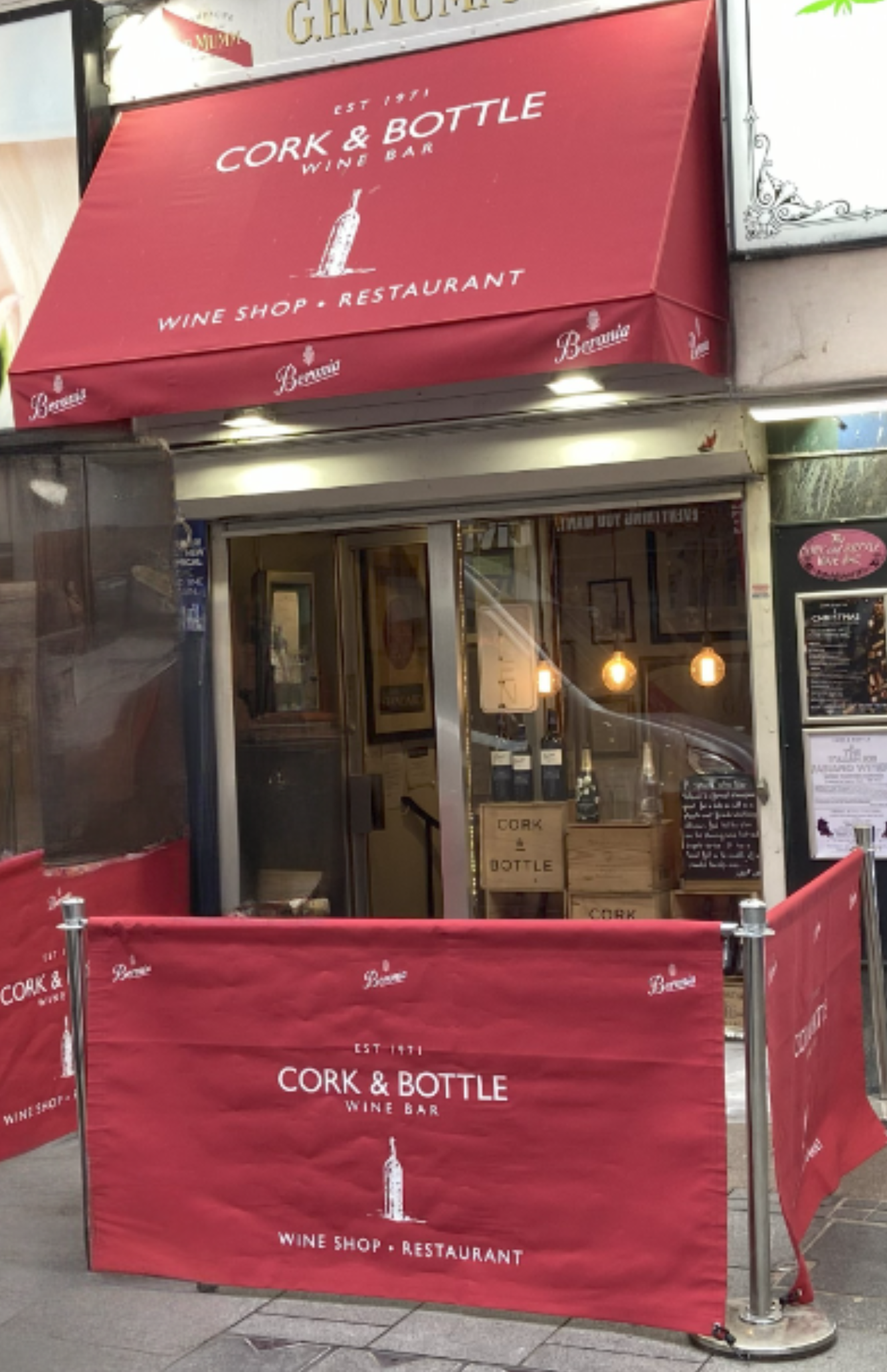 Front view of a shop with a newly recovered red awning and branded café barriers, showing how a small awning update can refresh and enhance a business frontage.